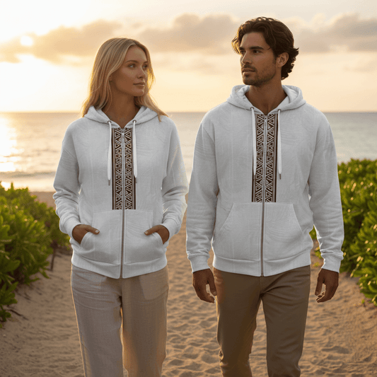 Man and woman wearing matching Islander zip hoodies with geometric tribal pattern walking on resort beach path at sunset