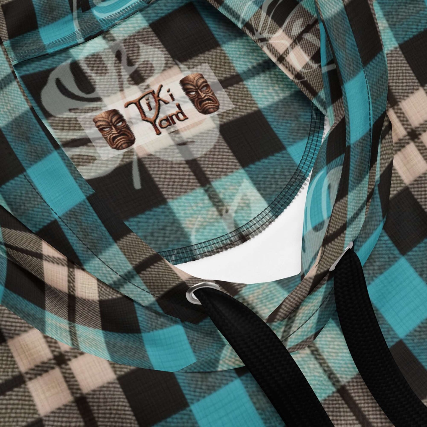 Close-up of a plaid hoodie with Tiki brand label and black drawstrings, highlighting unique Hawaiian-inspired design elements.