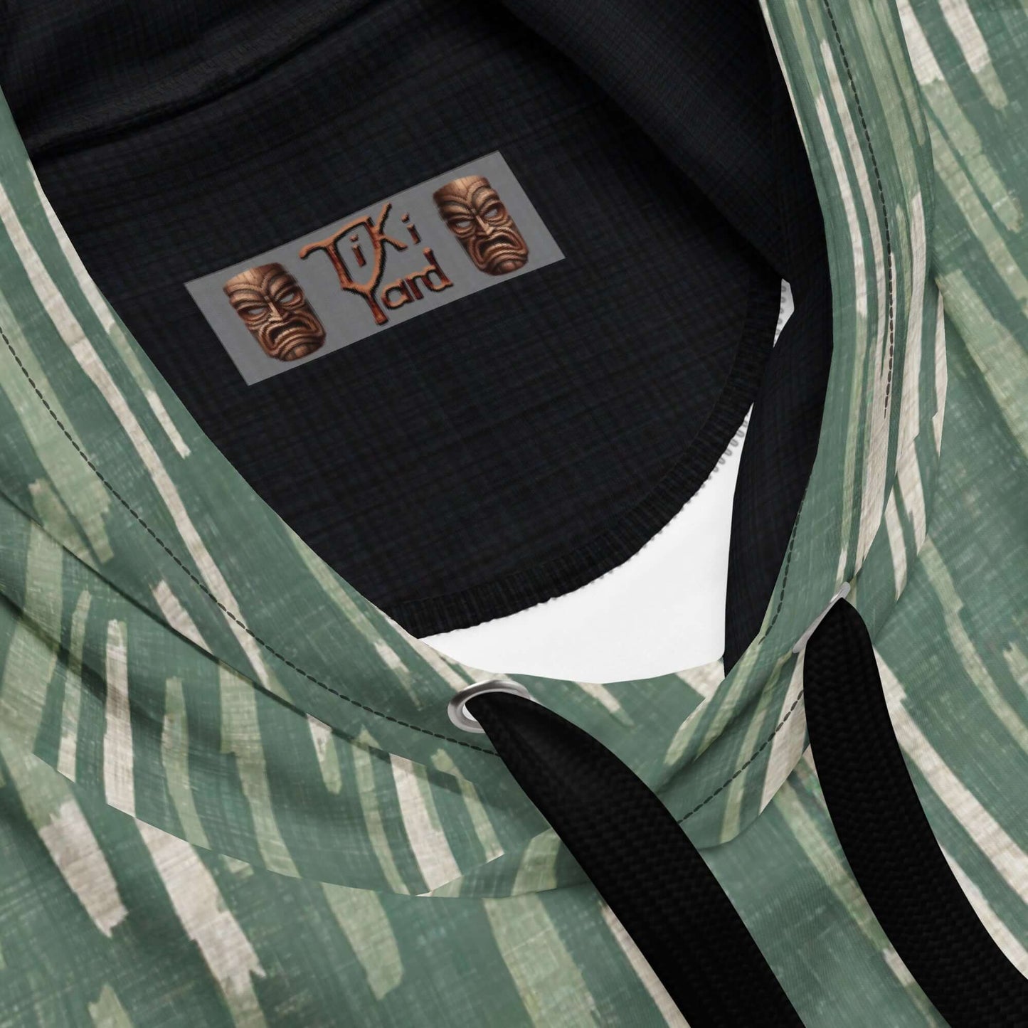 Close-up view of Tiki Nahele Hawaiian Hoodie showing intricate label design and stylish green pattern.