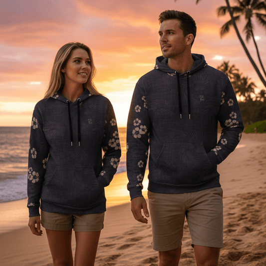 Couple wearing matching Tropical Eclipse pullover hoodies with hibiscus flowers on sleeves walking on Hawaiian beach at sunset