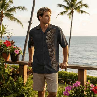 Man wearing Tiki Distortion Hawaiian shirt with dark charcoal base and carved tiki mask design at outdoor bar deck overlooking ocean