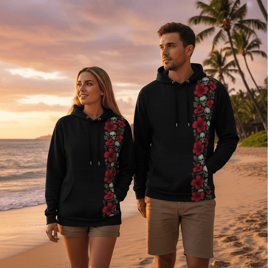 Couple wearing matching Skull Island pullover hoodies with skull and hibiscus stripe walking on Hawaiian beach at sunset
