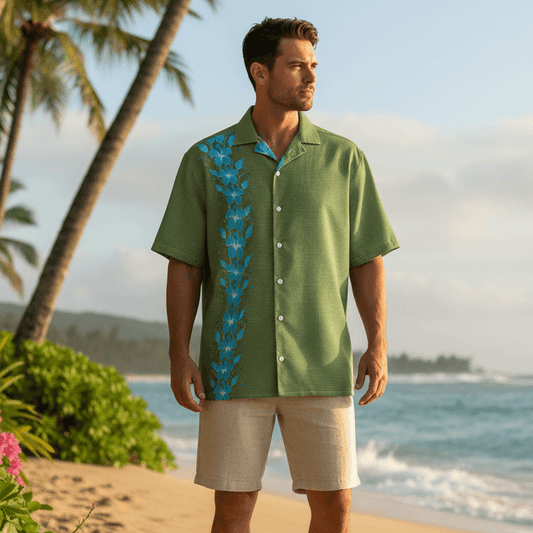Man wearing Verdant Aloha Hawaiian shirt with olive green base and turquoise blue hibiscus flowers at beachfront with palm trees