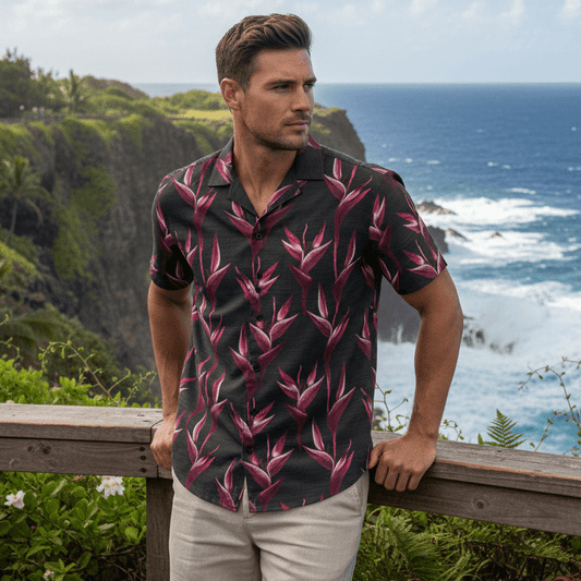 Man wearing Kauai Passion Hawaiian shirt with deep magenta heliconia flowers leaning against guard rail at dramatic coastal cliff overlook in Hawaii