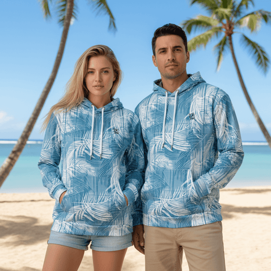 Couple wearing matching Blue Palms pullover hoodies with white palm fronds at Hawaiian beachfront